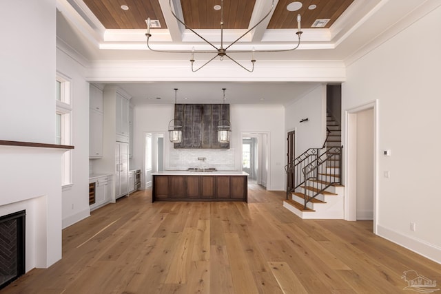 kitchen with light wood-style flooring, decorative light fixtures, a kitchen island with sink, light countertops, and crown molding