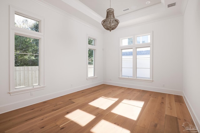 empty room with wood finished floors, a raised ceiling, visible vents, and crown molding