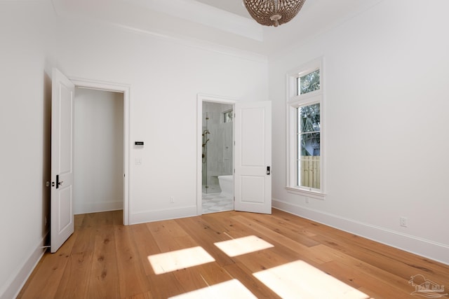 unfurnished bedroom with light wood-style floors, ensuite bath, baseboards, and a tray ceiling