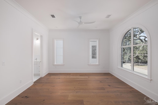 empty room with a healthy amount of sunlight, visible vents, ornamental molding, and dark wood-style flooring