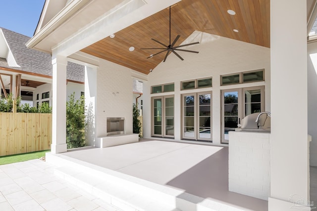 view of patio / terrace featuring exterior kitchen, a fireplace, fence, and a ceiling fan