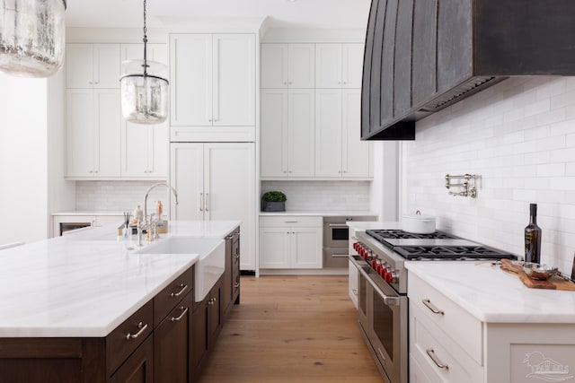 kitchen with range with two ovens, premium range hood, a sink, white cabinetry, and light wood-style floors