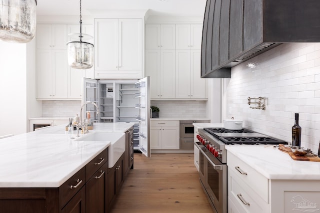 kitchen featuring range with two ovens, premium range hood, a sink, white cabinets, and light wood finished floors