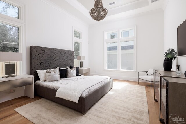 bedroom featuring light wood-style floors, a raised ceiling, visible vents, and ornamental molding