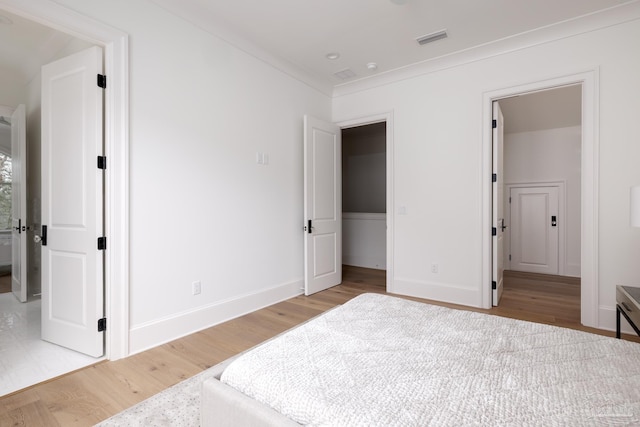 bedroom featuring light wood finished floors, baseboards, visible vents, and crown molding