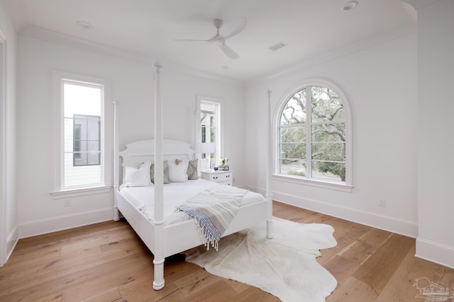 bedroom featuring light wood-type flooring, multiple windows, crown molding, and visible vents