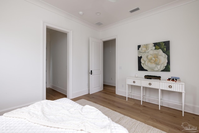 bedroom featuring baseboards, ornamental molding, visible vents, and light wood-style floors