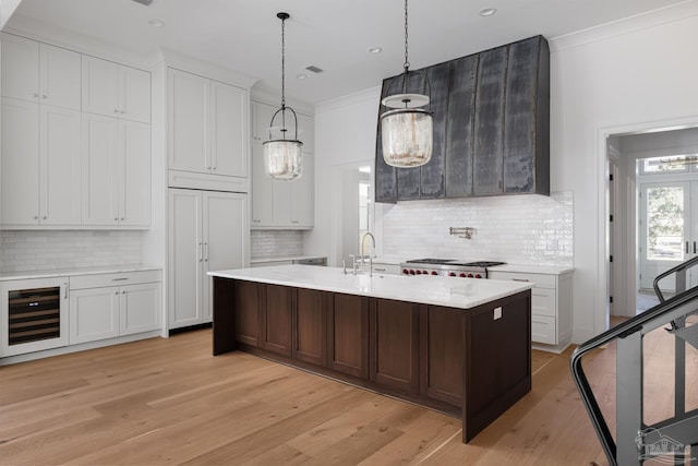 kitchen with light wood-style flooring, a center island with sink, white cabinetry, and crown molding