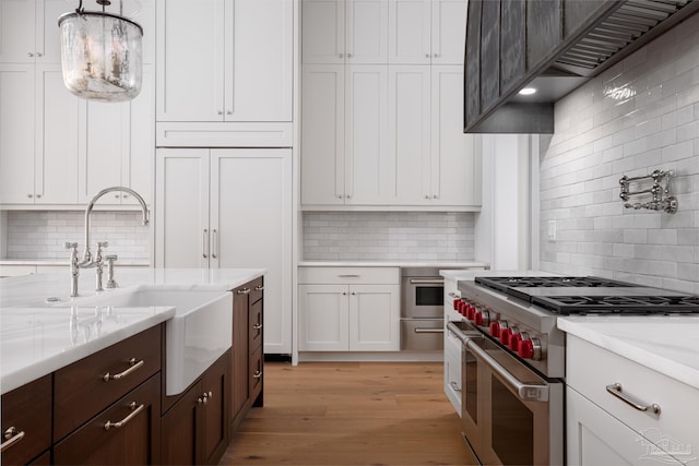 kitchen with pendant lighting, light wood finished floors, white cabinetry, a sink, and double oven range