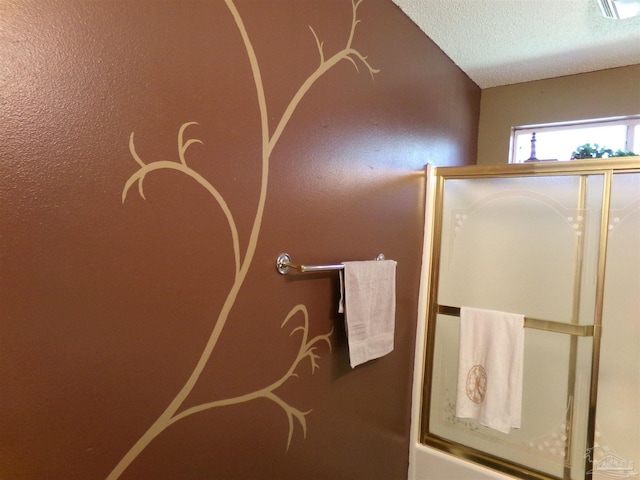 bathroom with a textured ceiling and enclosed tub / shower combo