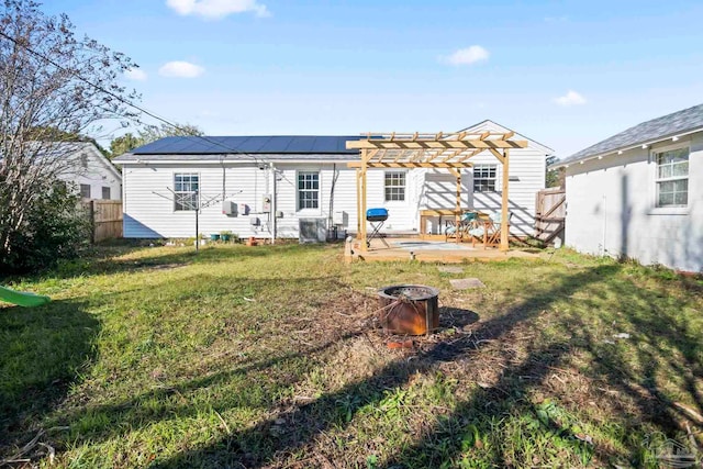 rear view of property featuring a pergola, a yard, and solar panels