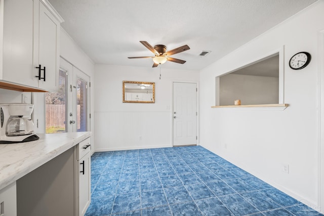 unfurnished room featuring a wainscoted wall, a textured ceiling, visible vents, and a ceiling fan