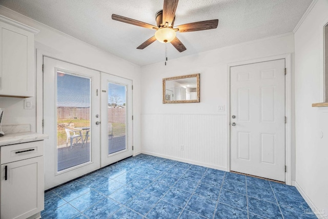 doorway featuring a ceiling fan, a wainscoted wall, ornamental molding, a textured ceiling, and french doors