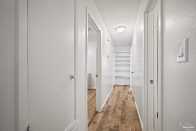 hall with light wood-type flooring, baseboards, and a textured ceiling