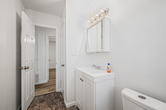 bathroom featuring a textured ceiling, toilet, visible vents, vanity, and stone finish floor