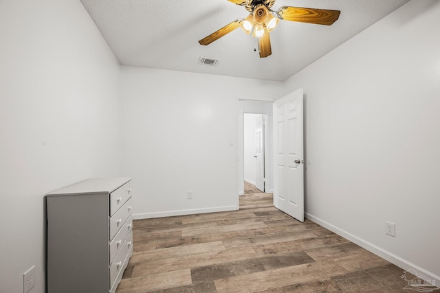 empty room with ceiling fan, light wood finished floors, visible vents, and baseboards