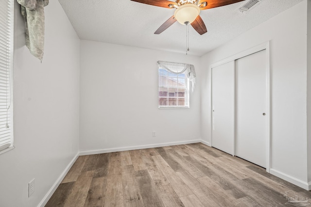 unfurnished bedroom featuring a textured ceiling, wood finished floors, visible vents, baseboards, and a closet