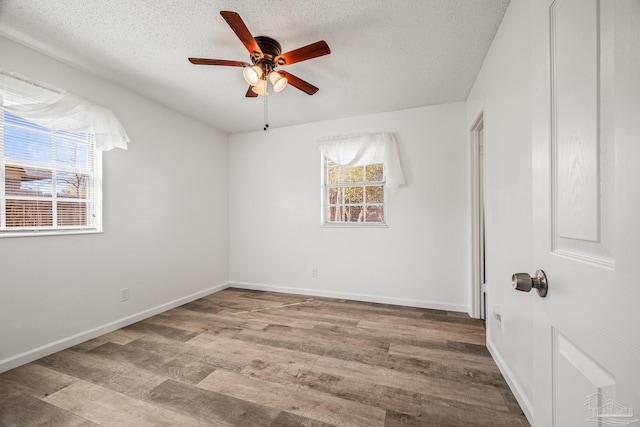 empty room with ceiling fan, a textured ceiling, baseboards, and wood finished floors