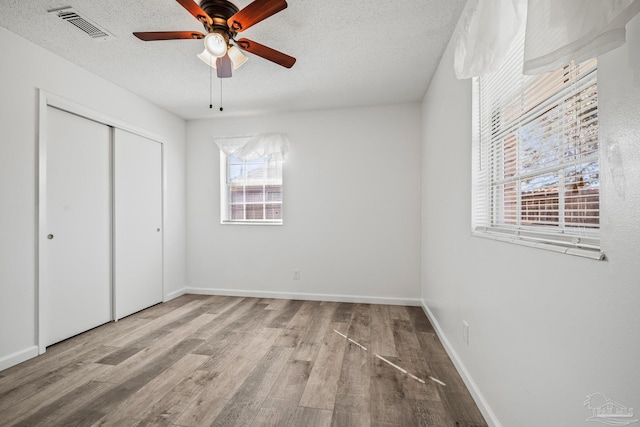 unfurnished bedroom with a closet, visible vents, a textured ceiling, wood finished floors, and baseboards