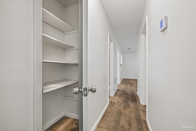 hallway with a textured ceiling, baseboards, and wood finished floors