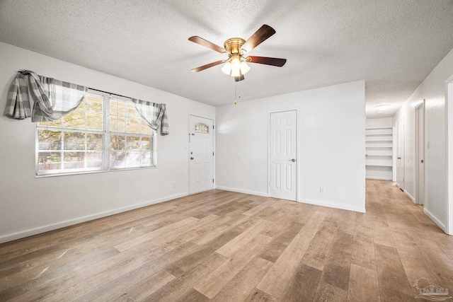 empty room with a textured ceiling, ceiling fan, light wood-style flooring, and baseboards