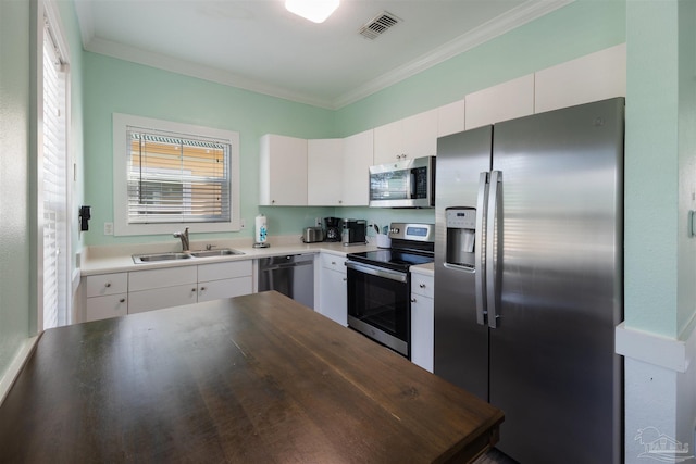 kitchen featuring stainless steel appliances, a sink, ornamental molding, and white cabinets