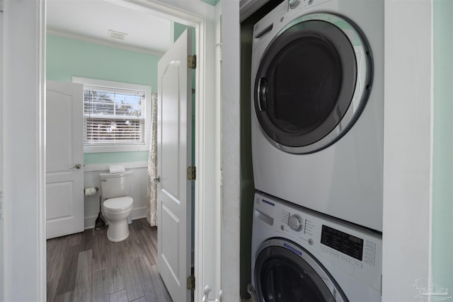 clothes washing area featuring stacked washer / drying machine and wood finished floors
