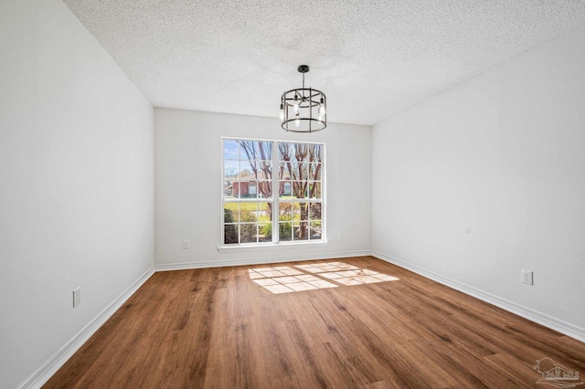 unfurnished dining area with baseboards, a textured ceiling, an inviting chandelier, and wood finished floors