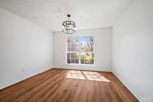 unfurnished dining area with a chandelier, a textured ceiling, baseboards, and wood finished floors