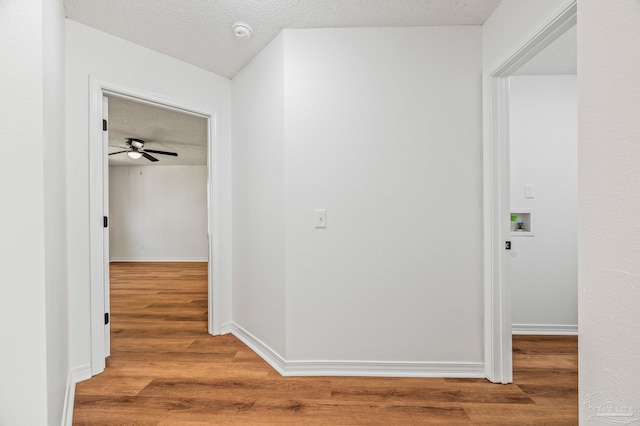 corridor with wood finished floors, baseboards, and a textured ceiling