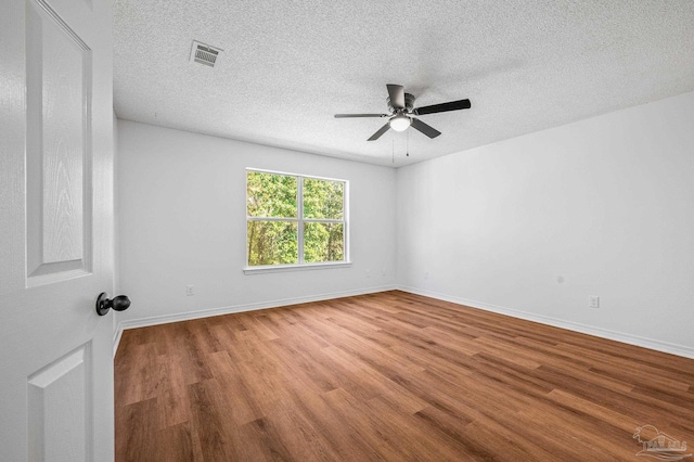 spare room featuring visible vents, a textured ceiling, baseboards, and wood finished floors