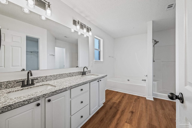 full bath featuring a textured ceiling, wood finished floors, a tub, and a sink