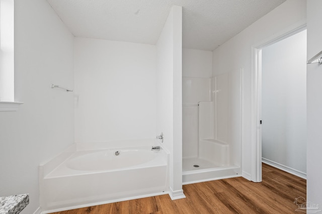 full bath with a bath, wood finished floors, a walk in shower, and a textured ceiling