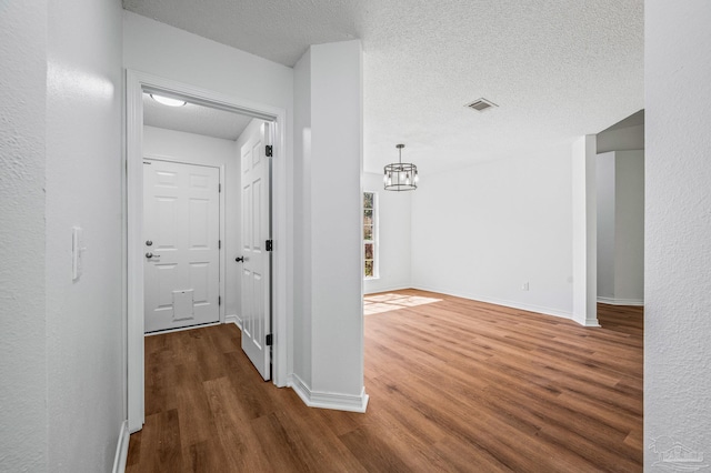 hallway featuring visible vents, baseboards, a textured ceiling, and wood finished floors