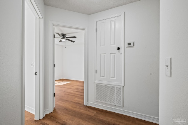 hallway featuring visible vents, a textured ceiling, baseboards, and wood finished floors