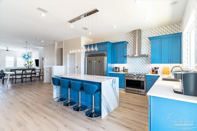 8169 White Sands Blvd, Navarre Beach, FL 32566 - kitchen featuring high end appliances, wall chimney exhaust hood, blue cabinets, a sink, and a center island