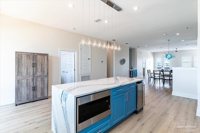 8169 White Sands Blvd, Navarre Beach, FL 32566 - kitchen featuring stainless steel microwave, light wood-type flooring, blue cabinetry, recessed lighting, and decorative light fixtures
