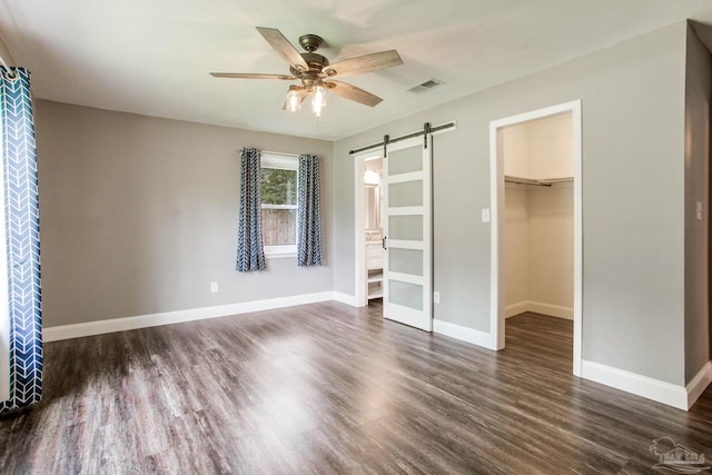 8818 Klondike Rd, Pensacola, FL 32526 - unfurnished bedroom featuring a barn door, dark wood finished floors, a walk in closet, a closet, and ceiling fan