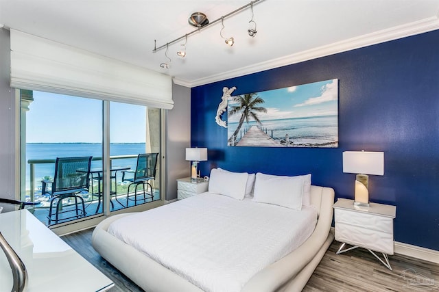 bedroom featuring track lighting, a water view, hardwood / wood-style floors, and ornamental molding