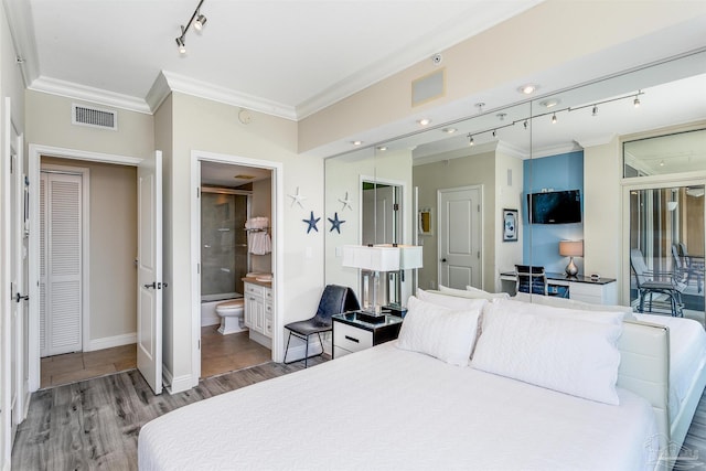 bedroom featuring ensuite bathroom, rail lighting, light wood-type flooring, and ornamental molding