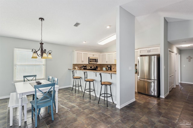 kitchen featuring lofted ceiling, decorative backsplash, appliances with stainless steel finishes, a notable chandelier, and kitchen peninsula