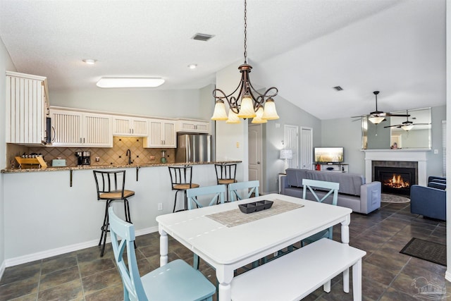 dining area with ceiling fan with notable chandelier, a textured ceiling, vaulted ceiling, sink, and a tiled fireplace