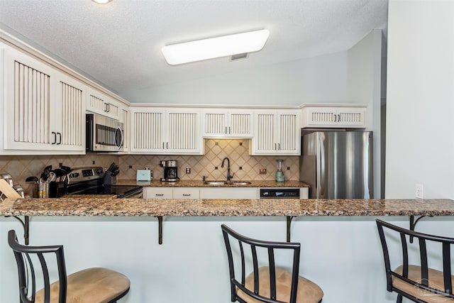 kitchen featuring kitchen peninsula, a kitchen breakfast bar, stainless steel appliances, sink, and lofted ceiling