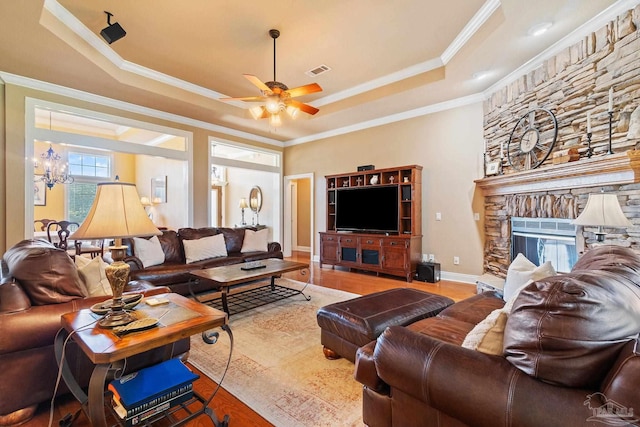 living room with ceiling fan with notable chandelier, wood-type flooring, a tray ceiling, and crown molding