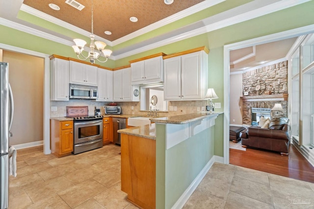 kitchen featuring white cabinets, stainless steel appliances, crown molding, and a raised ceiling