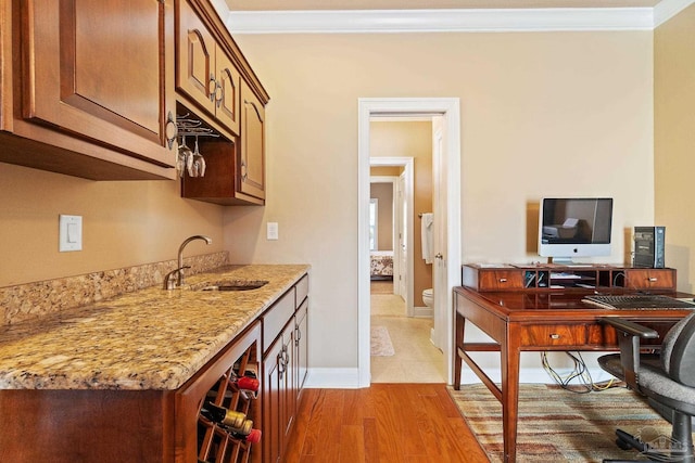 kitchen with ornamental molding, light stone counters, light hardwood / wood-style floors, and sink