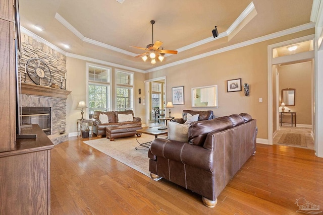 living room featuring light wood-type flooring, ornamental molding, a tray ceiling, and ceiling fan