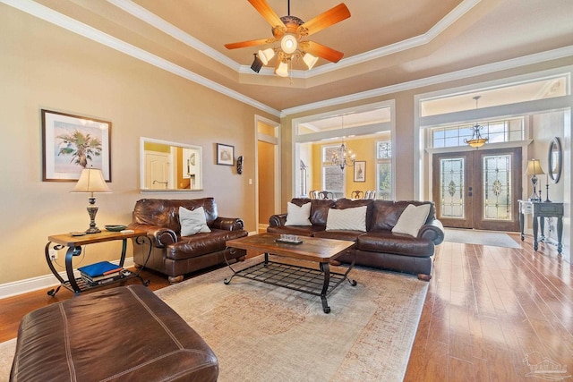 living room featuring ceiling fan with notable chandelier, a tray ceiling, hardwood / wood-style flooring, and crown molding