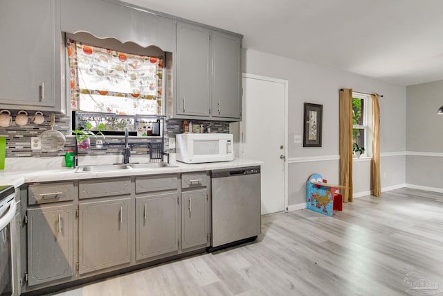 kitchen with gray cabinets, a sink, stainless steel dishwasher, backsplash, and white microwave