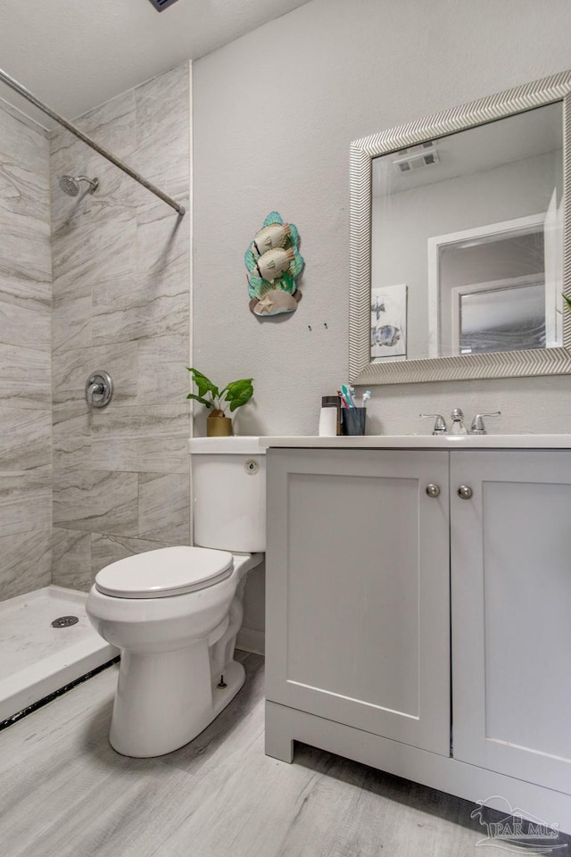 bathroom with vanity, wood finished floors, visible vents, a tile shower, and toilet